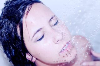 Rosto de mulher embaixo da água quente do chuveiro